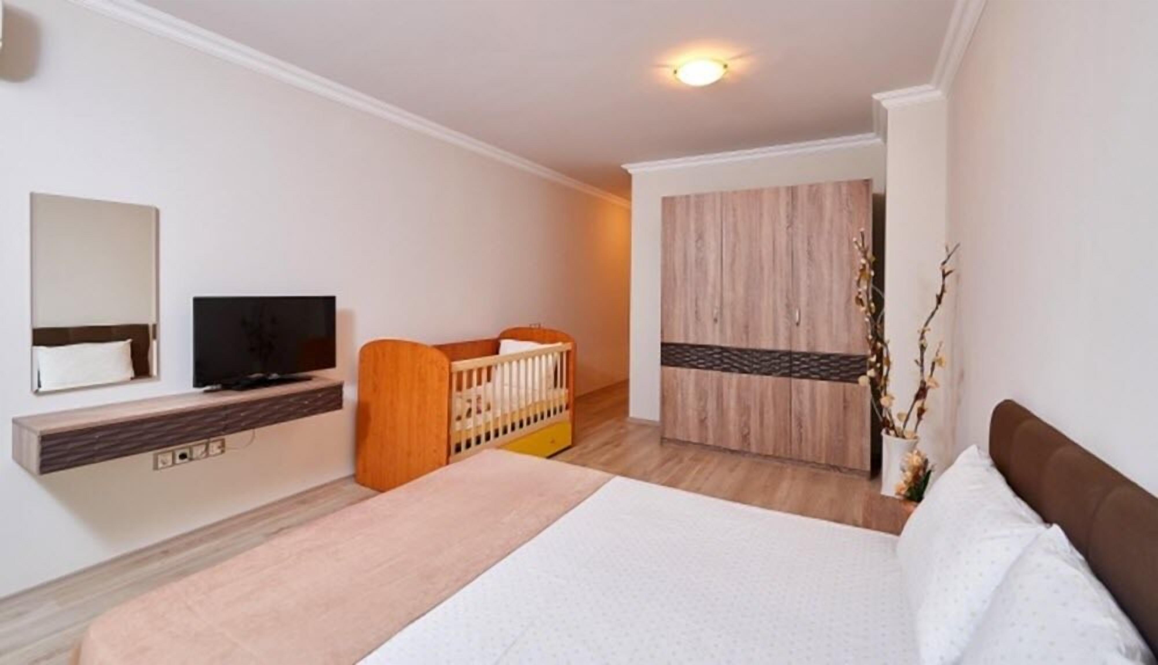 A bedroom with a bed, a TV, a crib, and a wardrobe.