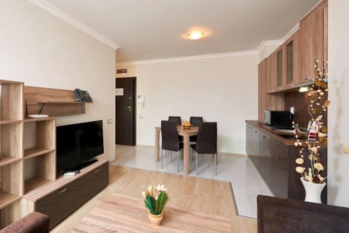 A modern living room with a TV, wooden shelves, a dining table, and a kitchen area with cabinets.