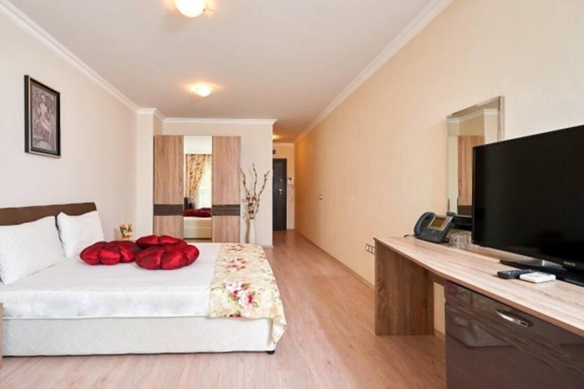 A hotel room with a bed, a desk with a flat-screen TV, and a mirror.