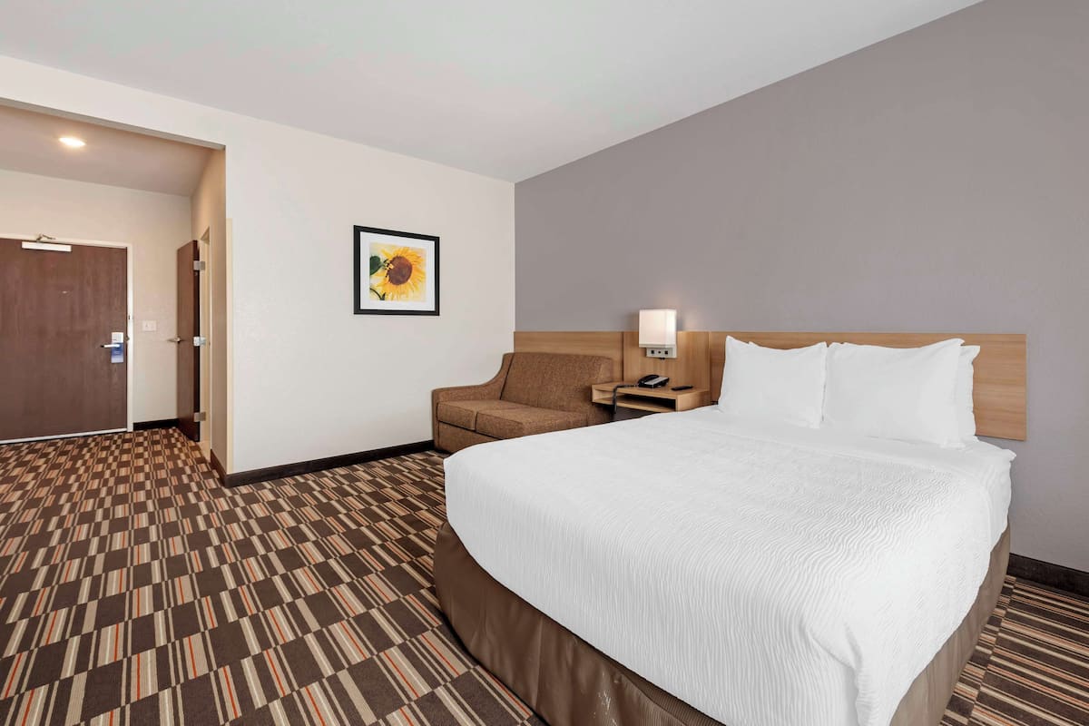 A hotel room with a large bed, a chair, a nightstand, and a wall-mounted lamp.