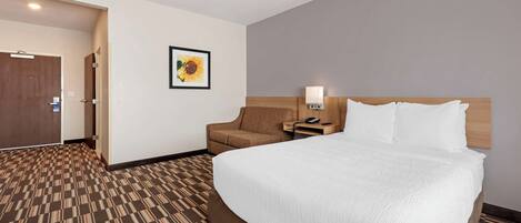 A hotel room with a large bed, a chair, a nightstand, and a wall-mounted lamp.