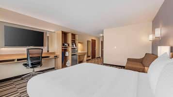 A hotel room with a large bed, a desk with a flat-screen TV, a microwave, a mini-fridge, and a seating area with a sofa and armchair.