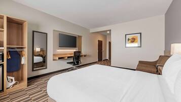 Una habitación de hotel con una cama grande, un escritorio con silla, un televisor montado en la pared y un armario.
