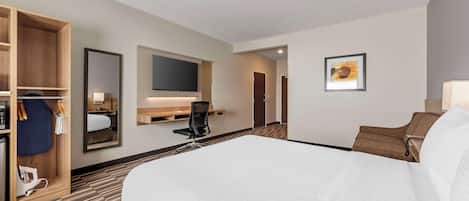 A hotel room with a large bed, a desk with a chair, a TV mounted on the wall, and a wardrobe.