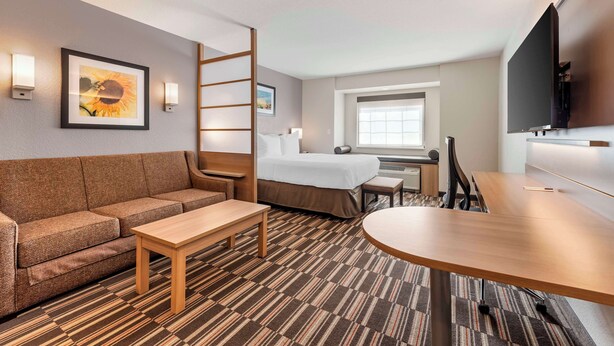 Ein Hotelzimmer mit einer Couch, einem Bett, einem Schreibtisch, einem Fernseher und einem Fenster.
