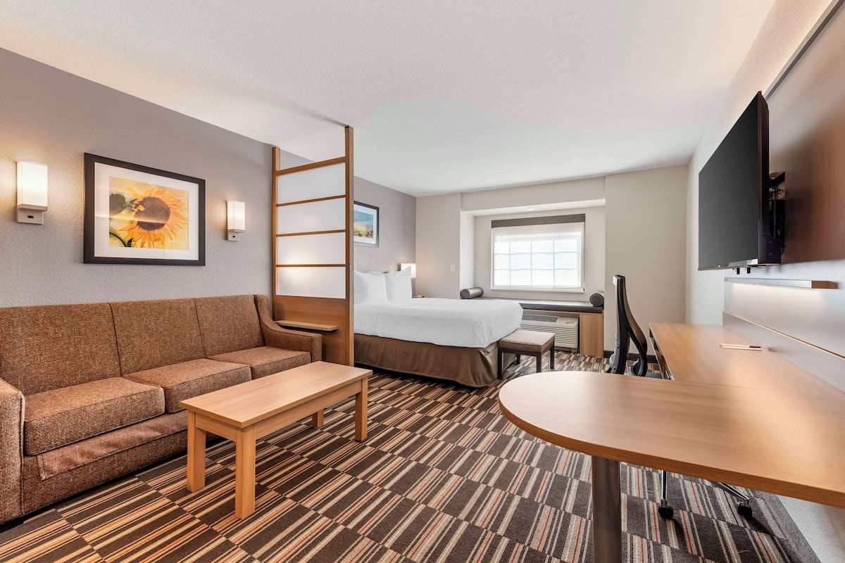 A hotel room with a sofa, a bed, a desk, a TV, and a window.