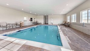 Ein Hallenbad mit gefliestem Boden, einer Poolleiter und Liegestühlen am Rand.