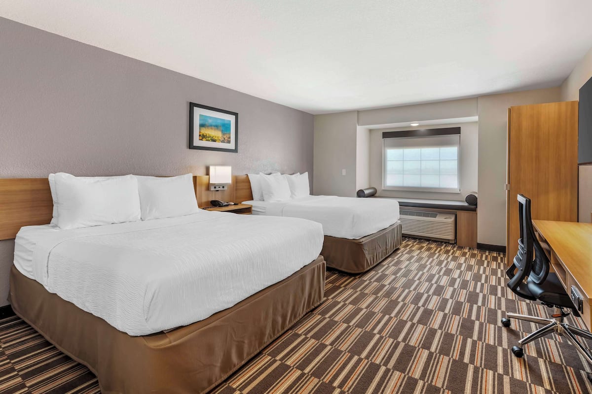 A hotel room with two beds, a desk, a chair, a window, and a picture on the wall.