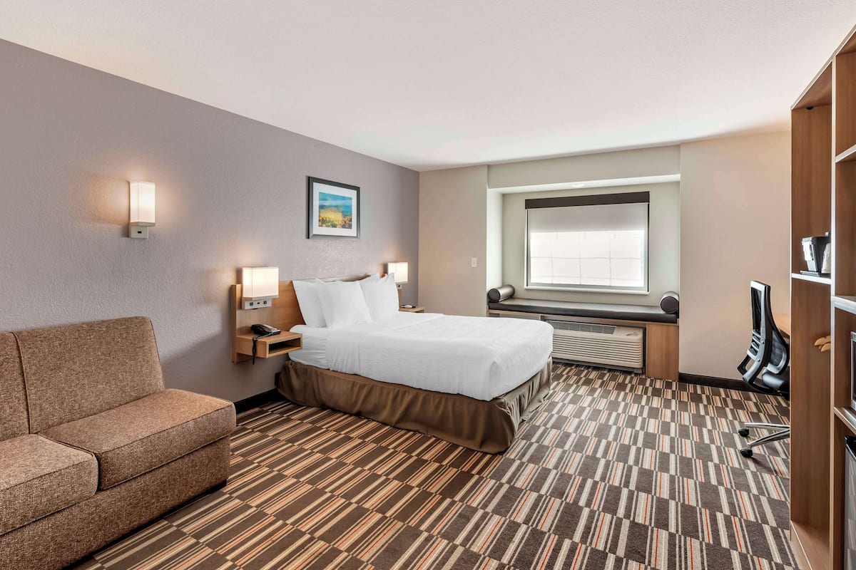 A hotel room with a bed, a sofa, a desk, a lamp, a picture on the wall, and a window.