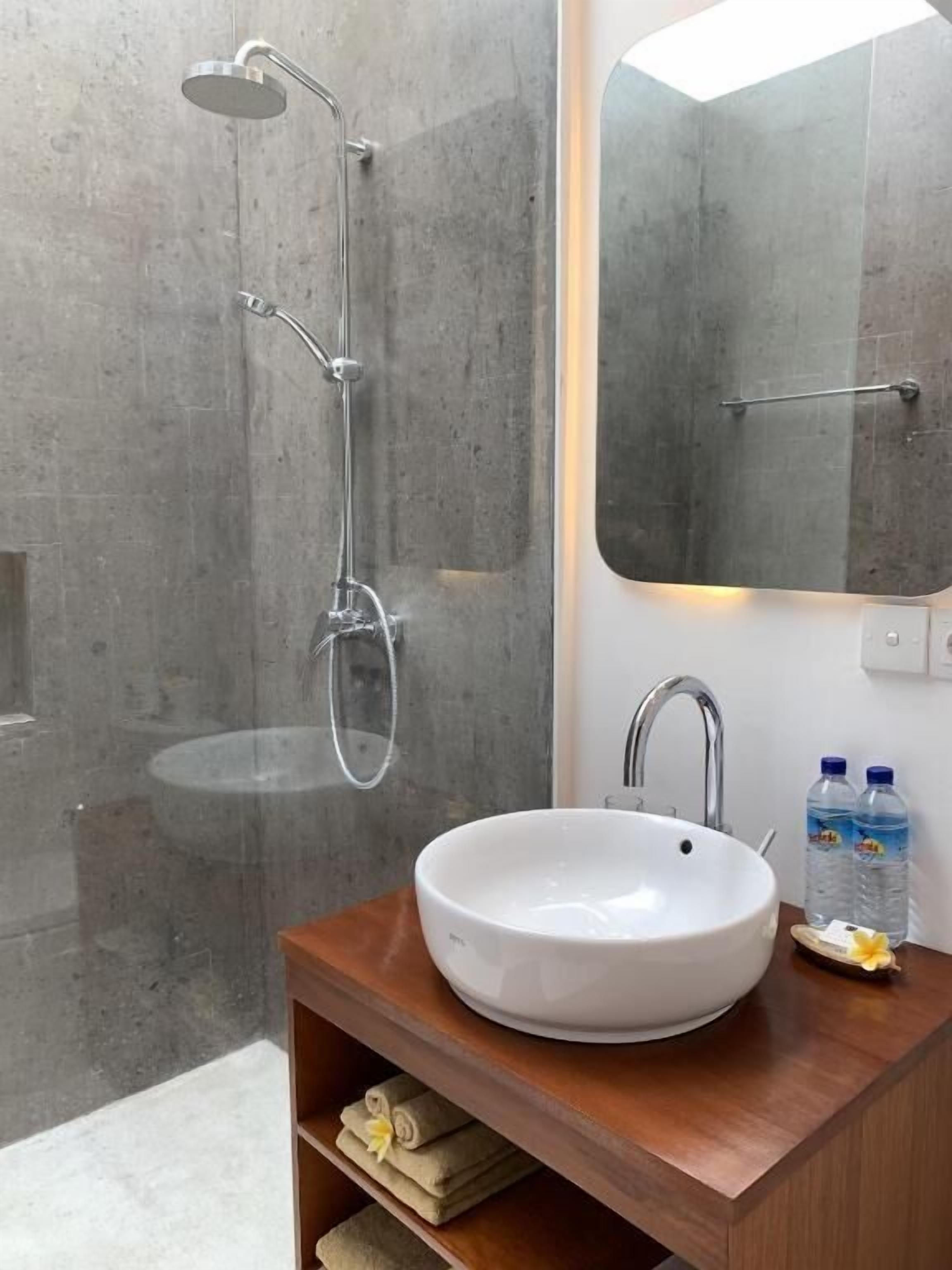 Ein modernes Badezimmer mit einer freistehenden Dusche, einem großen Spiegel und einem Holzwaschtisch mit weißem Waschbecken.