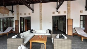 A covered outdoor seating area with wicker furniture, a central coffee table, and stone pillars. - Bale Solah Lombok Holiday Resort (Batu Layar)