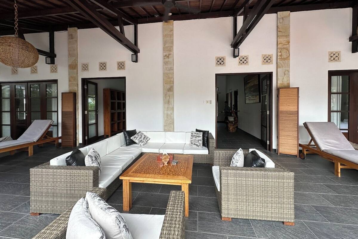 A covered outdoor seating area with wicker furniture, a central coffee table, and stone pillars.