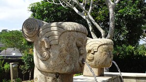 A stone fountain with two sculptures, one of a face and one of a head, in a garden setting. - Bale Solah Lombok Holiday Resort (Batu Layar)