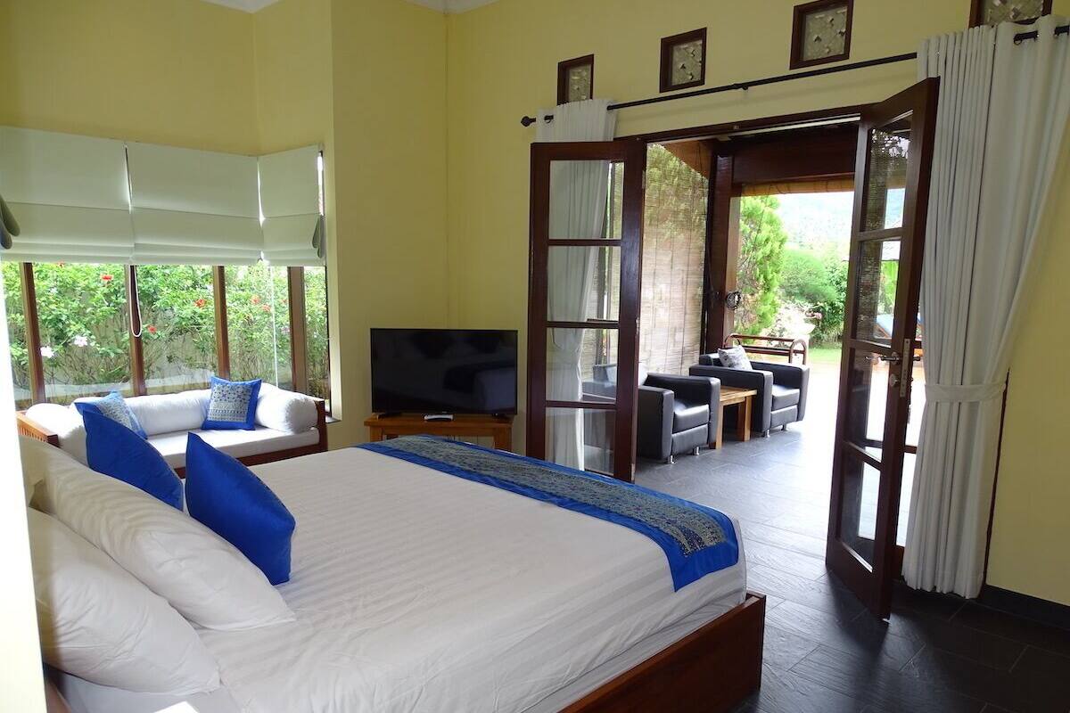 A bedroom with a large bed, a TV, and a view of the garden through an open door.