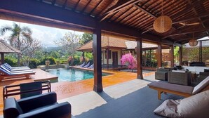 A covered outdoor area with a pool, lounge chairs, and seating. - Bale Solah Lombok Holiday Resort (Batu Layar)