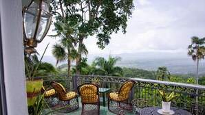 A balcony with wicker chairs and a table, surrounded by lush greenery and a scenic view. - Hotel Santo Cerro Natural Park  (La Vega)