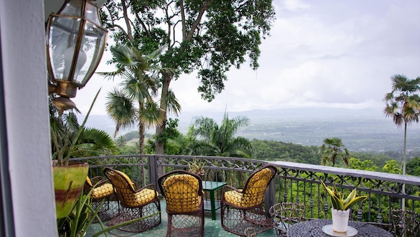 A balcony with wicker chairs and a table, surrounded by lush greenery and a scenic view. - Hotel Santo Cerro Natural Park  (La Vega)