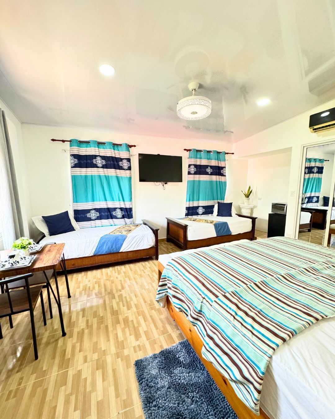 A hotel room with two beds, a desk, a chair, a television, and a ceiling fan.