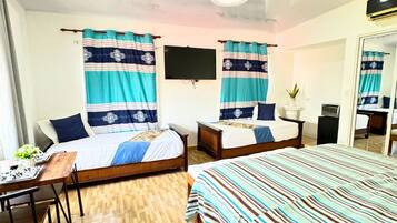 A hotel room with two beds, a desk, a chair, a television, and a ceiling fan.
