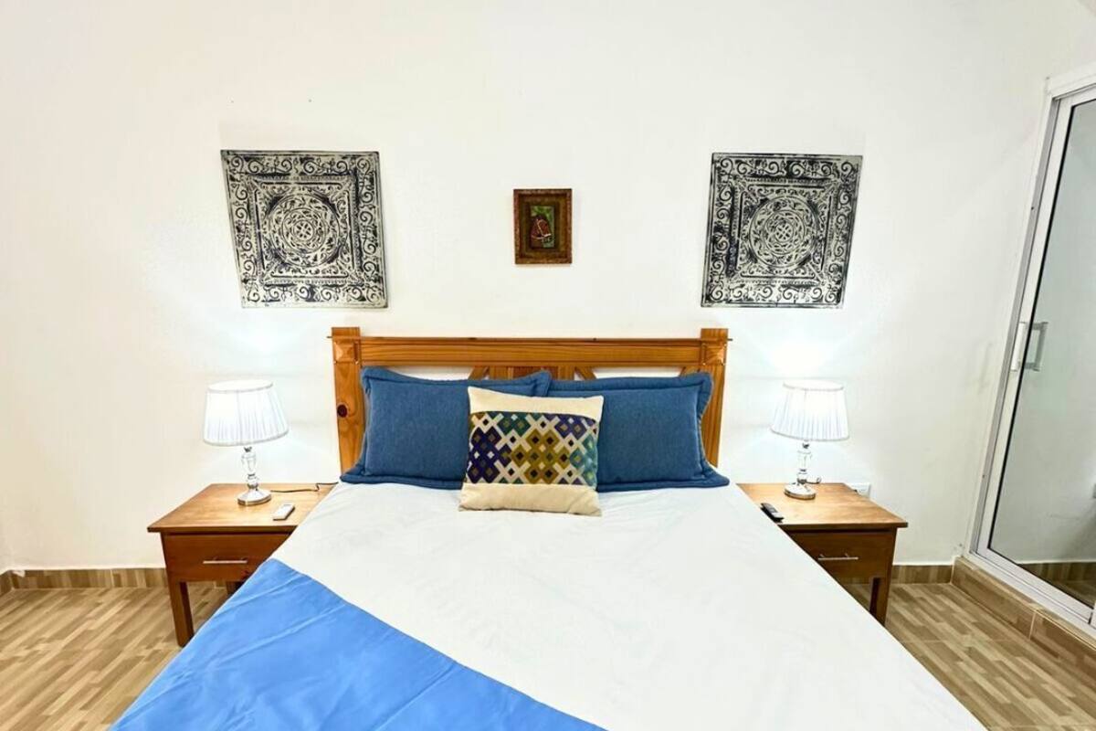Ein Schlafzimmer mit einem Bett, zwei Nachttischen, einem hölzernen Kopfteil, Wandbildern mit Muster und einer Klimaanlage.