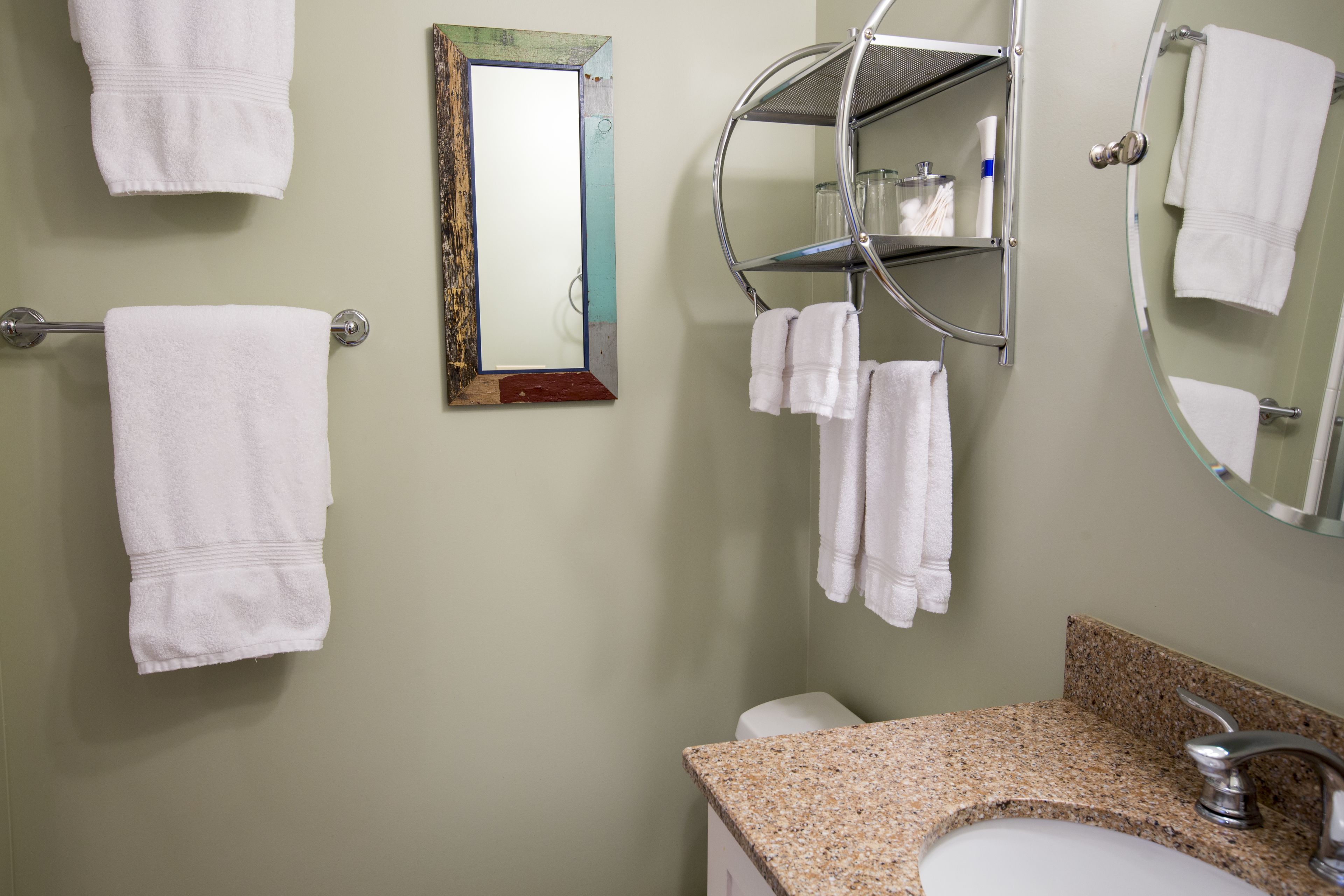 A bathroom with a granite countertop sink, a toilet, and multiple white towels hanging on towel racks.