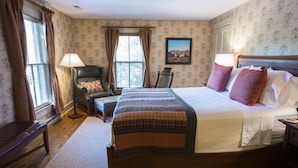 A bedroom with a large bed, a chair, a desk, and a window with curtains.