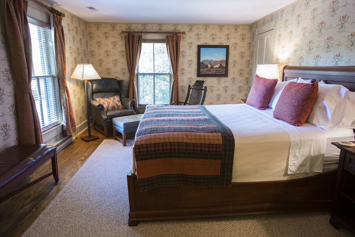 A bedroom with a large bed, a chair, a desk, and a window with curtains.