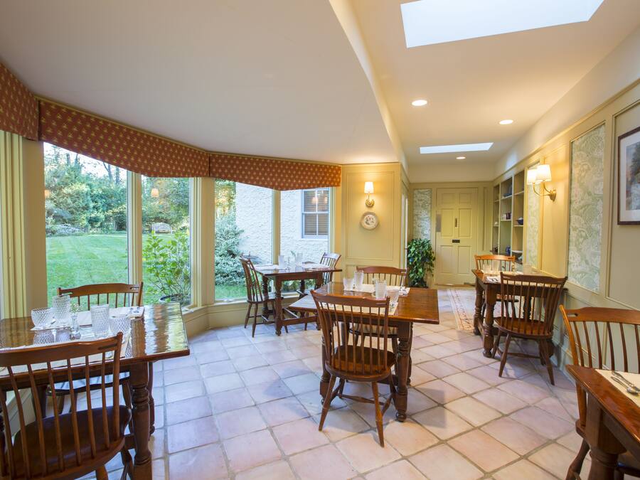 Un espace repas avec des tables et des chaises en bois, de grandes fenêtres donnant sur l’extérieur et une lucarne au plafond.