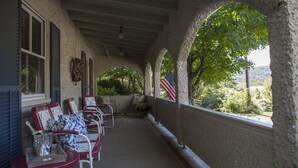 A covered porch with red and white chairs, a small table with a bottle and glasses, and an American flag.