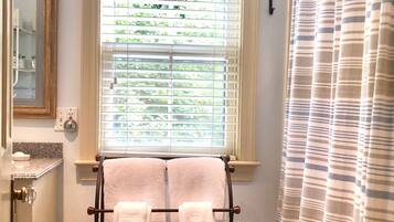 A bathroom with a window, a towel rack with two towels, a shower curtain, a mirror, and a sink with a soap dispenser.
