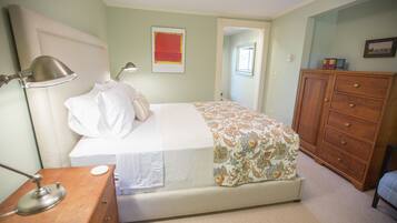 A bedroom with a bed, bedside lamp, wooden dresser, and a door leading to another room.