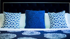 A bed with a dark headboard, two patterned pillows, and a blue knitted throw.
