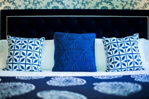 A bed with a dark headboard, two patterned pillows, and a blue knitted throw.