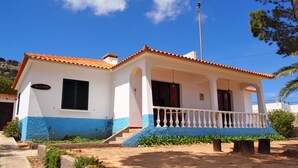 Una casa de dos pisos con fachada blanca y azul, techo de tejas y un balcón con barandilla blanca.
