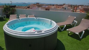 A rooftop terrace with a hot tub surrounded by lounge chairs, overlooking a cityscape with mountains in the distance. - Apartamentos 525 (Los Alcázares)