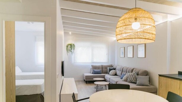 A modern living room with a sofa, a dining table, and a hanging light fixture. - Apartamentos 525 (Los Alcázares)