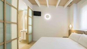 A hotel room with a large bed, a television mounted on the wall, and a bathroom visible through a glass door. - Apartamentos 525 (Los Alcázares)