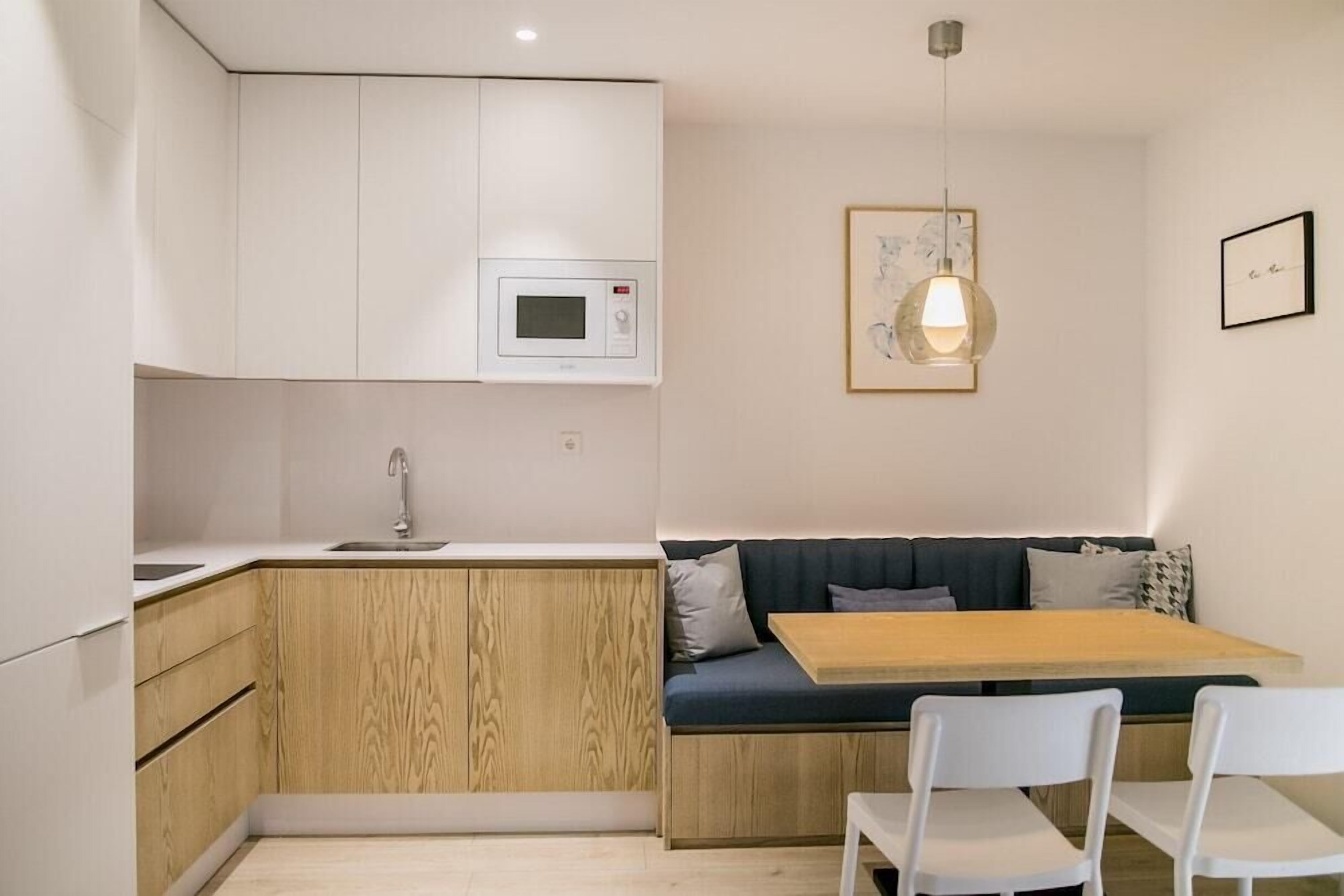 Eine kompakte Küche mit Mikrowelle, Spüle und einem Holzkasten. Es gibt einen Essbereich mit Tisch und Stühlen, und eine Schrankwand mit einer Couch.