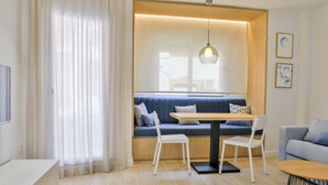 A modern living room with a wooden floor, a blue sofa with cushions, a white dining table with two chairs, a grey sofa, and a wooden coffee table. - Apartamentos 525 (Los Alcázares)