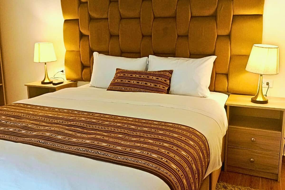 A hotel room with a tufted headboard, a large bed with patterned bedding, two bedside tables with lamps, and a wooden nightstand.