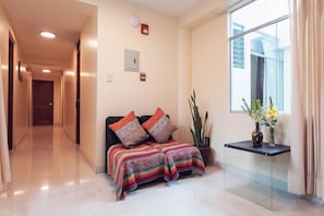 A hotel lobby with a reception desk, a sofa with patterned cushions, a potted plant, and a window with curtains. - Hotel Las Quenas (Cusco)