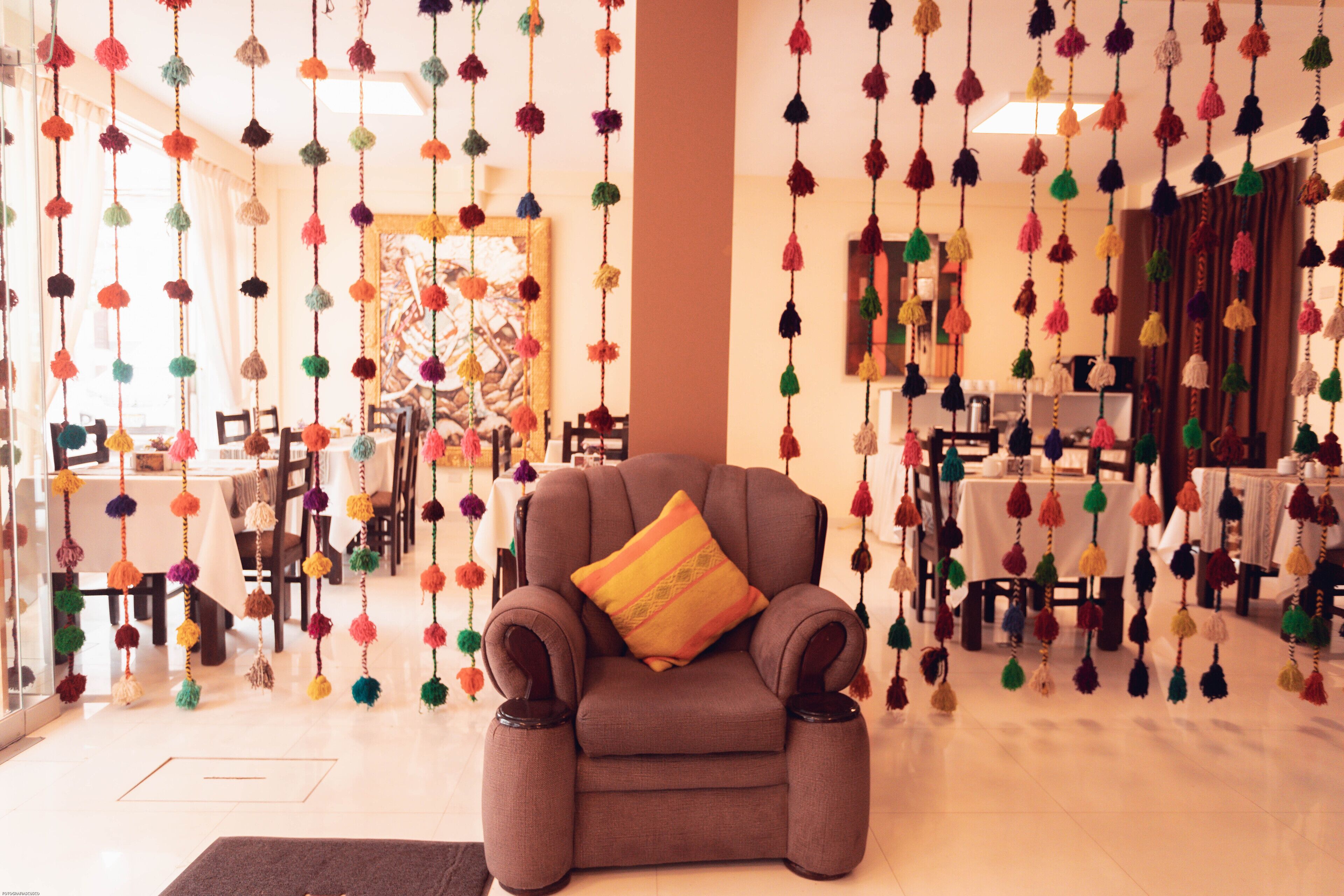 A room with a brown armchair, colorful hanging decorations, and a dining area with tables and chairs.