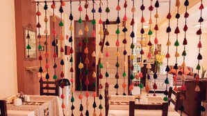 A dining area with a table set for two, a mirror on the wall, and colorful tassels hanging from the ceiling. - Hotel Las Quenas (Cusco)