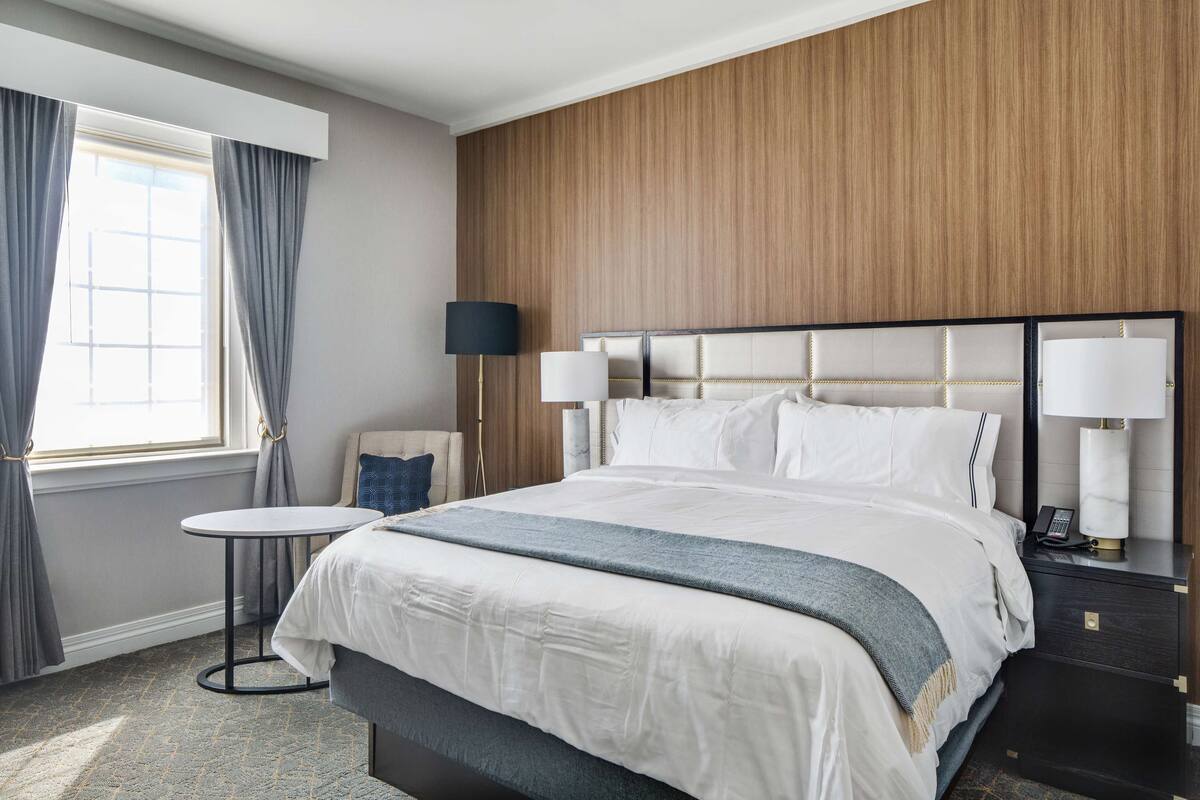 Habitación de hotel con una cama grande, una mesita redonda pequeña, una lámpara y una mesita de noche con un teléfono.
