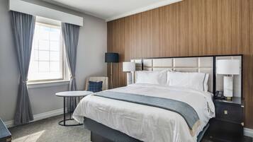 Quarto de hotel com uma cama grande, uma mesinha redonda, uma luminária e uma mesa de cabeceira com telefone.