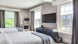 A hotel room with two beds, a desk with a flat-screen TV, a chair, and large windows.