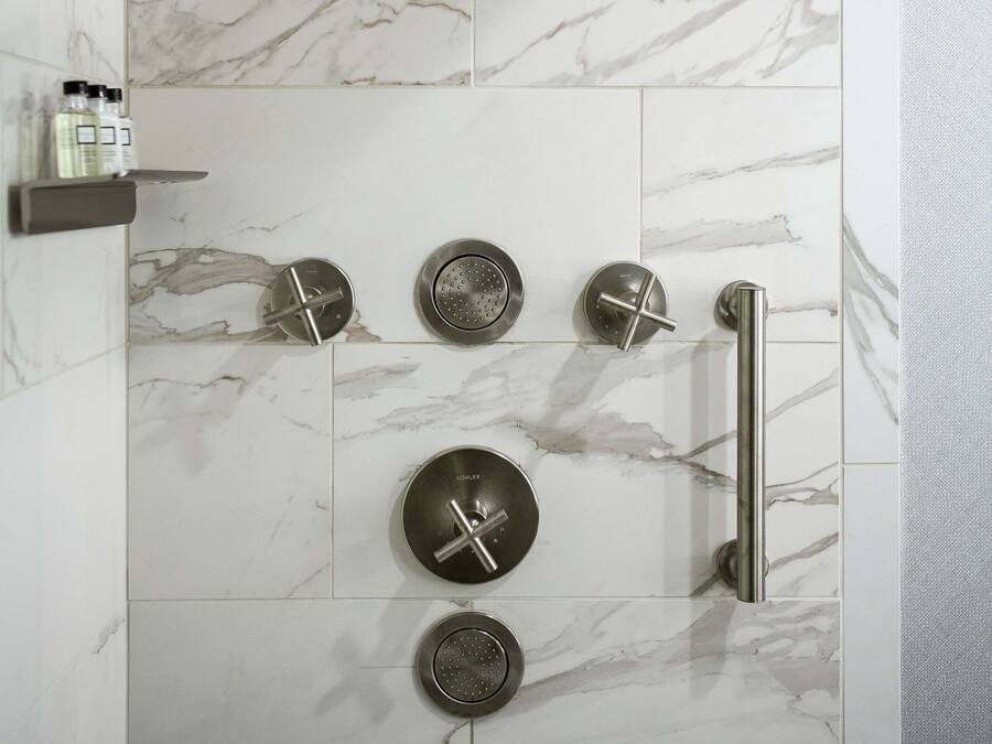 Eine moderne Dusche mit mehreren Bedienfeldern und einer Handbrause, vor einer Wand aus Marmorfliesen.
