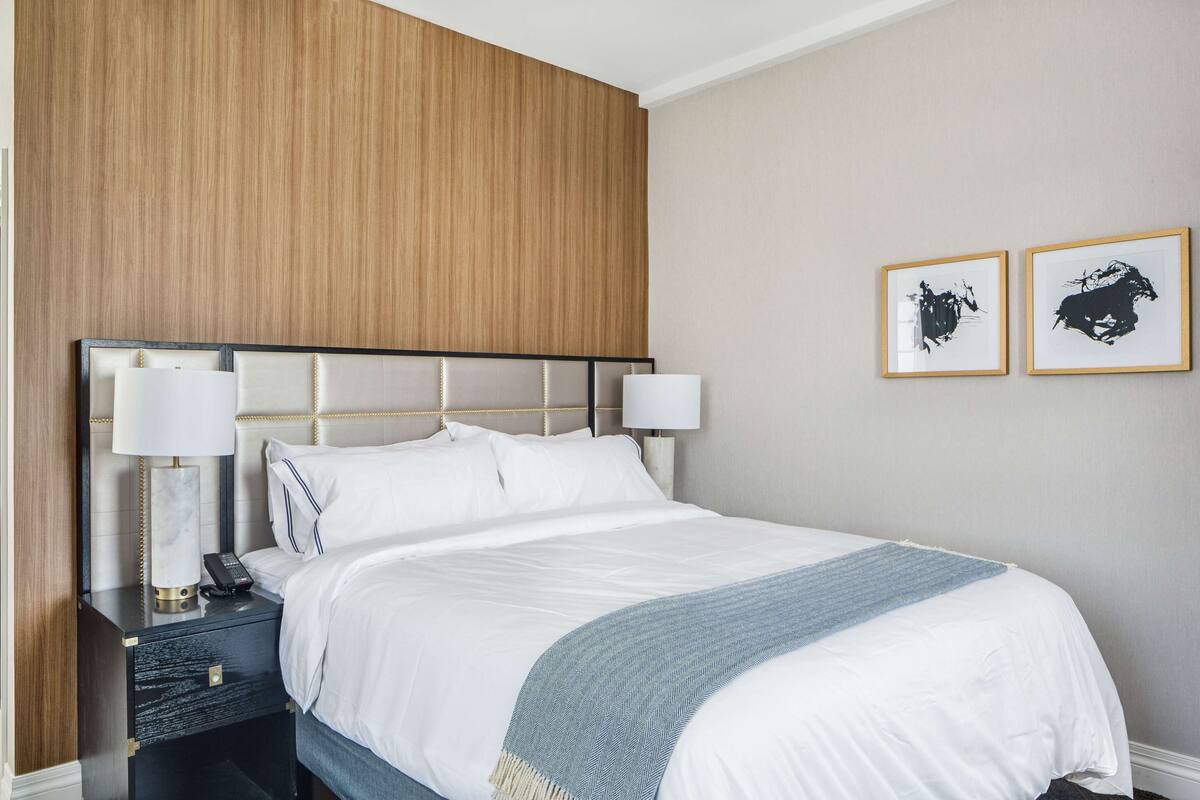 Una habitación de hotel con una cama grande, dos mesitas de noche, una silla y una lámpara.