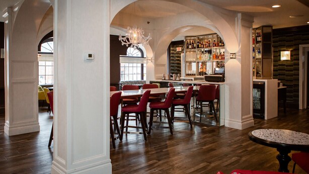 A spacious bar area with wooden flooring, red chairs, and a bar counter.