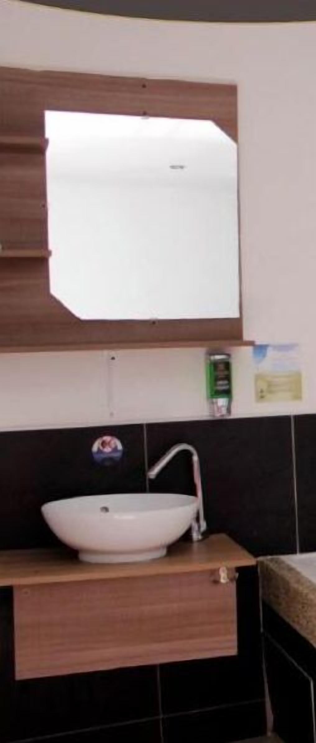 A bathroom with a white sink, a mirror above it, and a dark tiled backsplash.